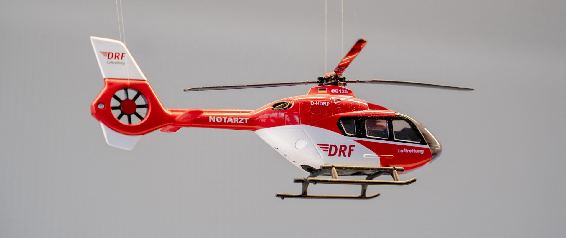 Das Bild zeigt ein Modell eines DRF Luftrettungshelikopters. Die DRF Luftrettung ist eine deutsche Organisation, die sich auf Luftrettung und medizinische Notfallversorgung spezialisiert hat. Der Helikopter ist in charakteristischem Rot und Weiß lackiert und trägt die Aufschrift "DRF"—ein Hinweis auf die Organisation.