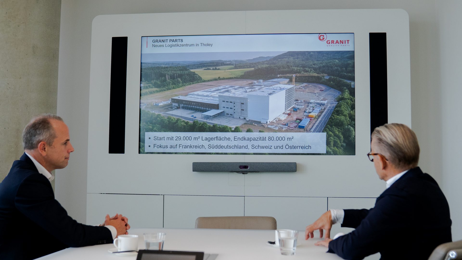 Ein Präsentationsbild von einer Gebäudestruktur auf einem Bildschirm, das möglicherweise Teil eines Meetings ist, bei dem Bauprojekte oder Unternehmensentwicklungen diskutiert werden.