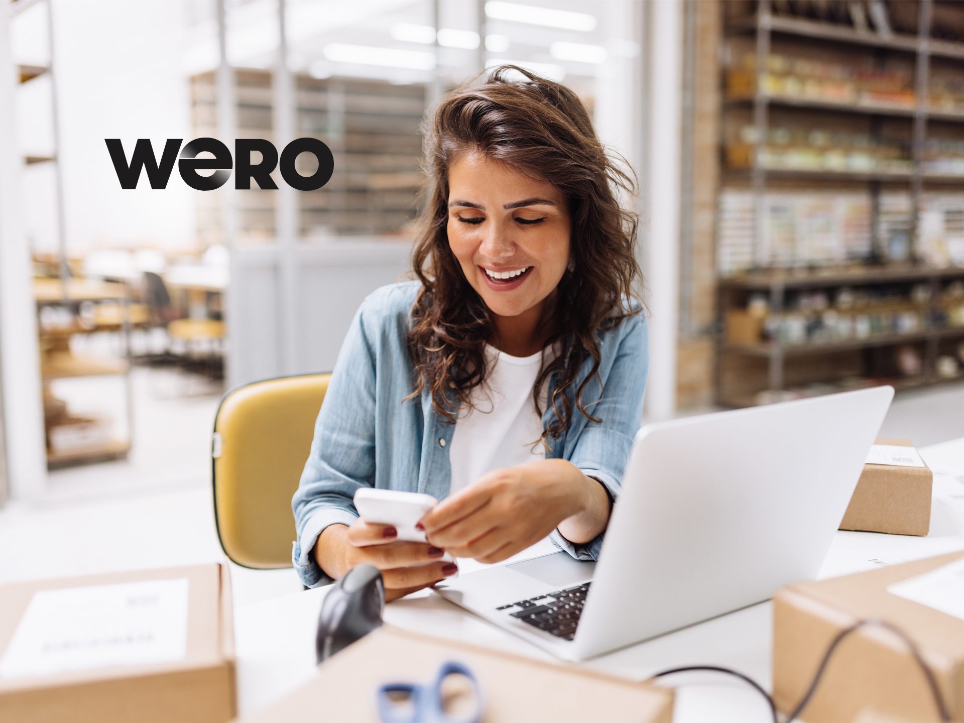 Die Szene mit einer Person in einem hellen Büroraum mit einem Laptop und Versandverpackungen. Das Logo "WERO" ist zu sehen.